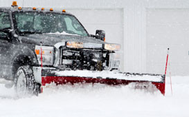 A truck is plowing the snow in front of a garage.